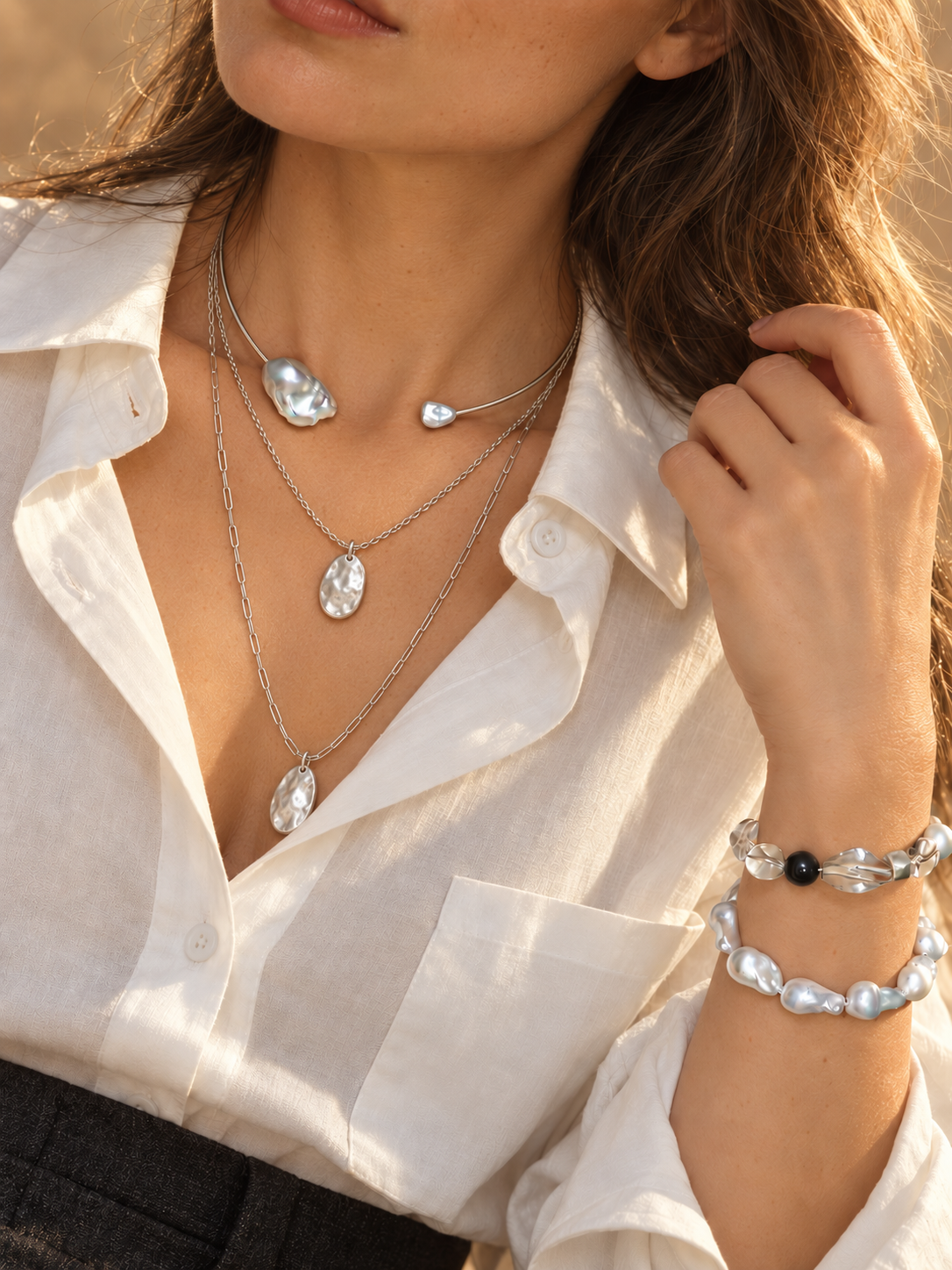 Layered pearl necklaces and bracelets worn with a cream blouse in golden sunlight