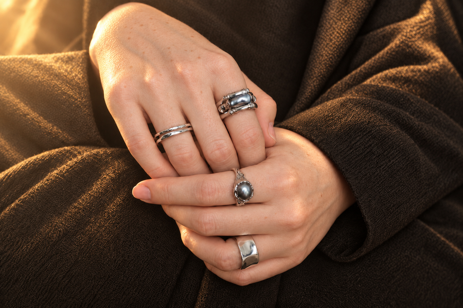 Four silver rings worn on two clasped hands in golden sunlight