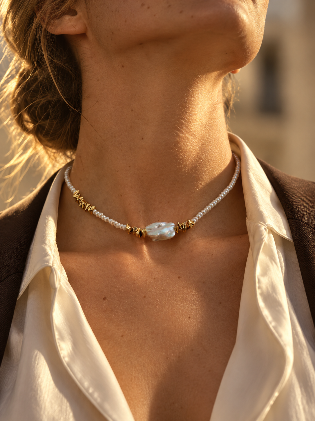 Small white pearls, irregular gold-tone spacers and a central baroque pearl at the neckline in golden sunlight
